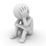 Auf dem Boden sitzendes Männchen das sich den Kopf hält. Das Bild soll einen leidenden Eindruck machen, so wie man es von starken Kopfschmerzen kennt.