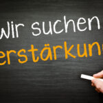 Auf eine Schiefertafel wird geschrieben: Wir suchen Verstärkung. Zum Ausdruck soll gebracht werden, dass wir weitere Mitarbeiter suchen.