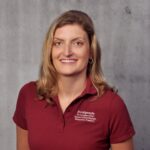 Rebecca Raddatz, Blondhaarige Frau in einem roten Shirt mit Aufschrift Frauengesundheit vor einer grauen Wand