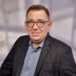 Dr. Michael Sroka, dunkelhaariger Mann mit Brille in blauem Hemd und Sakko vor grauem Hintergrund