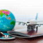 Auf einem Tisch befinden ein Stethoskop, Reisepass, ein Spielflugzeug und ein Globus, Hinweis für Gesundheit und Reiseversicherung